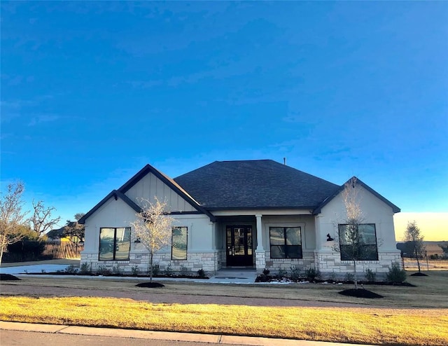 modern farmhouse style home with a front yard, stone siding, and roof with shingles