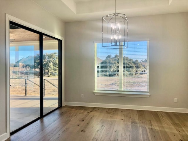 unfurnished dining area featuring baseboards, a chandelier, and wood finished floors