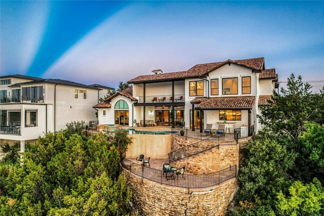 1208 Watercliffe Dr, Lago Vista, TX 78645 - back of house at dusk featuring a patio, stucco siding, a balcony, and an outdoor pool