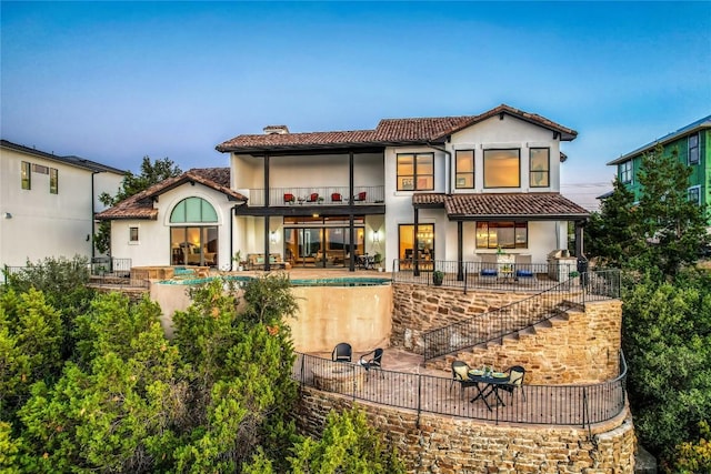 back of house featuring a balcony, a tile roof, stairway, a chimney, and a patio area