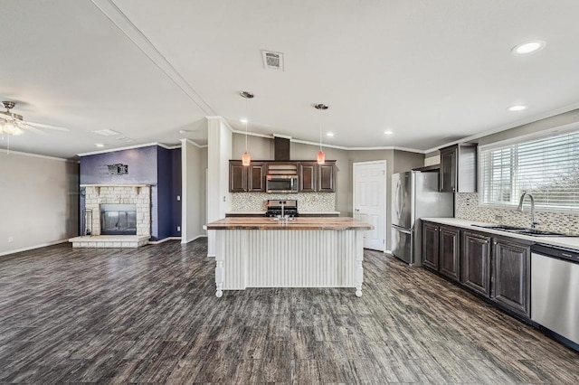 kitchen with butcher block countertops, appliances with stainless steel finishes, a sink, open floor plan, and crown molding