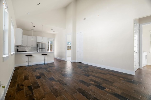 unfurnished living room with baseboards, high vaulted ceiling, and dark wood-style flooring