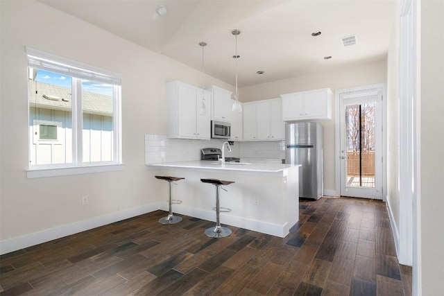 kitchen featuring stainless steel appliances, a peninsula, dark wood-style flooring, a sink, and decorative backsplash