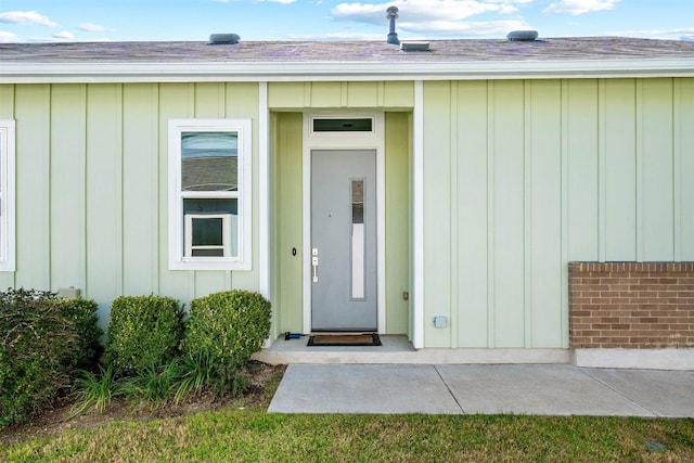 property entrance featuring a shingled roof, board and batten siding, and brick siding