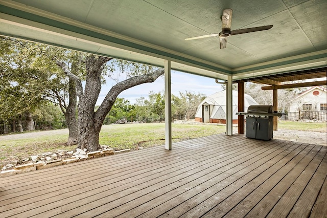 wooden terrace featuring a ceiling fan, area for grilling, an outbuilding, a yard, and a shed