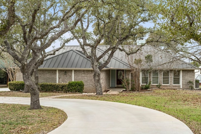 view of front facade featuring metal roof, brick siding, driveway, and a front lawn