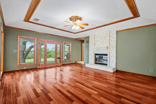 unfurnished living room with a tray ceiling, a brick fireplace, wood finished floors, and visible vents