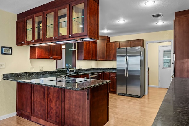 kitchen with reddish brown cabinets, visible vents, appliances with stainless steel finishes, a sink, and a peninsula