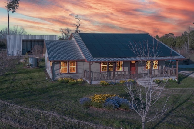 view of front facade with a porch, roof mounted solar panels, metal roof, and a lawn