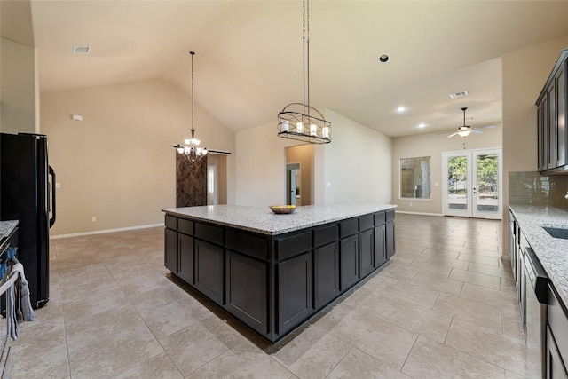 kitchen featuring a center island, visible vents, freestanding refrigerator, light stone countertops, and dark cabinets