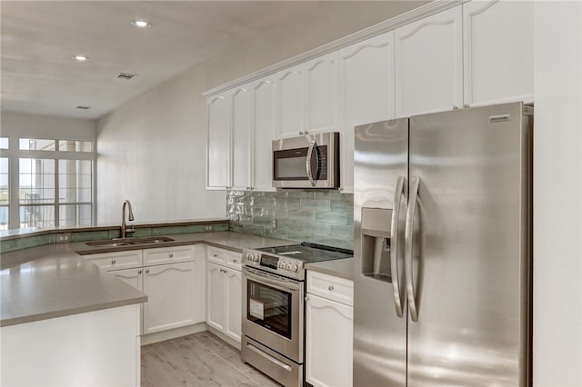 kitchen with stainless steel appliances, a sink, white cabinets, backsplash, and a peninsula