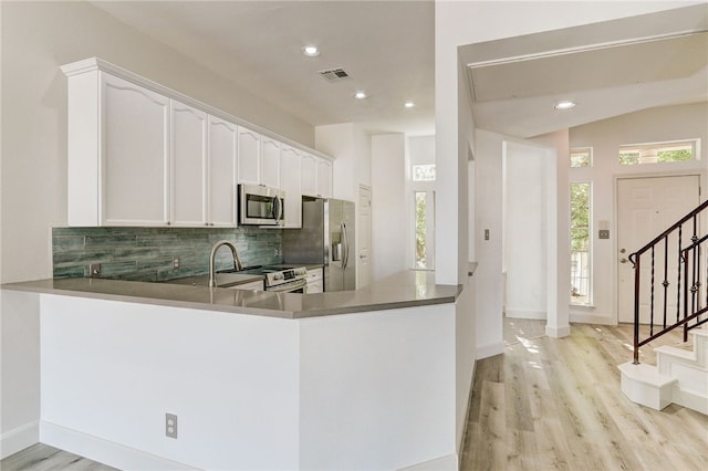 kitchen with appliances with stainless steel finishes, light wood-type flooring, backsplash, white cabinets, and a peninsula
