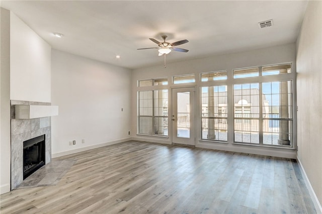 unfurnished living room featuring ceiling fan, wood finished floors, baseboards, and a tiled fireplace