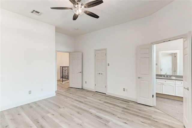 unfurnished bedroom featuring light wood finished floors, baseboards, a sink, connected bathroom, and a high ceiling