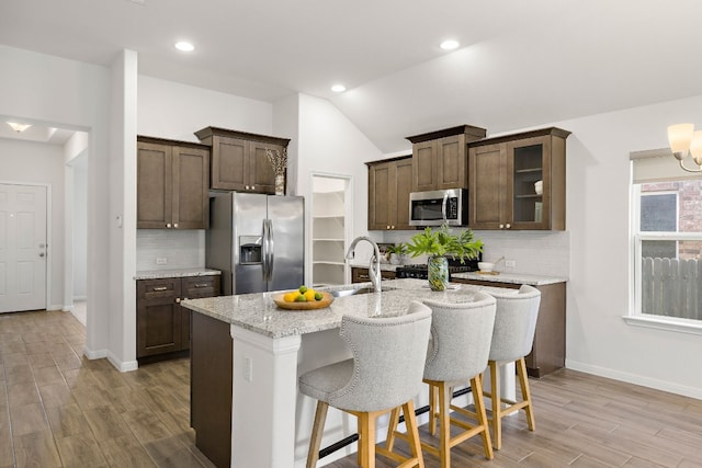 kitchen featuring lofted ceiling, light wood-style flooring, appliances with stainless steel finishes, dark brown cabinets, and a sink