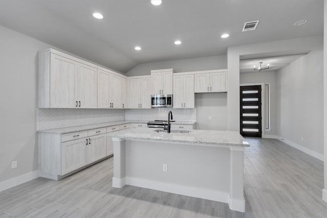 kitchen featuring tasteful backsplash, a center island with sink, visible vents, light stone countertops, and stainless steel appliances