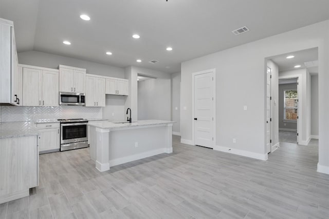 kitchen featuring a center island with sink, stainless steel appliances, visible vents, backsplash, and a sink