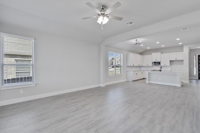 unfurnished living room with light wood-style floors, baseboards, visible vents, and a ceiling fan