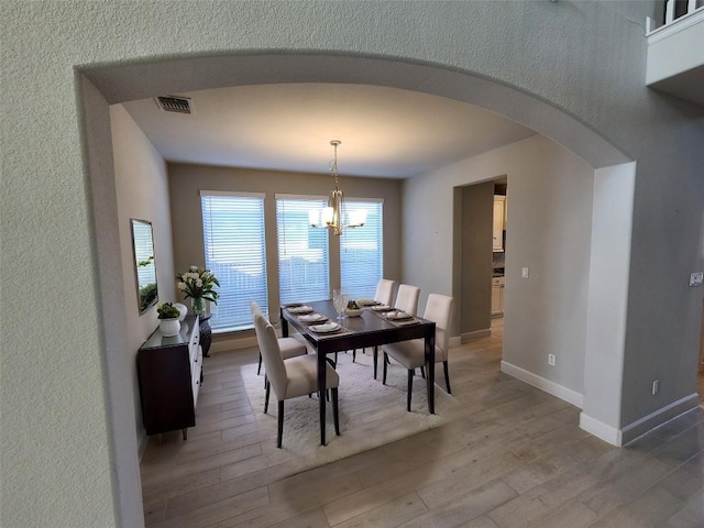 dining space with arched walkways, visible vents, baseboards, and wood finished floors