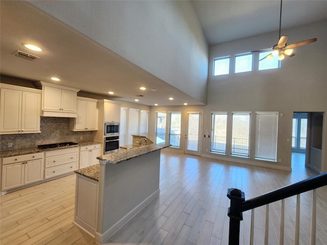 kitchen featuring tasteful backsplash, open floor plan, black cooktop, and light wood-style flooring