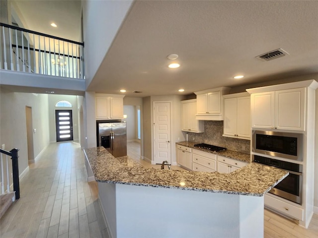 kitchen featuring stainless steel appliances, visible vents, white cabinets, backsplash, and light wood finished floors