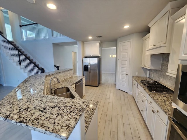 kitchen featuring tasteful backsplash, appliances with stainless steel finishes, light stone countertops, light wood-style floors, and a sink