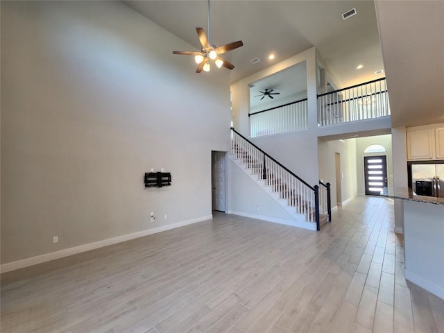 unfurnished living room with light wood-type flooring, visible vents, baseboards, and stairs