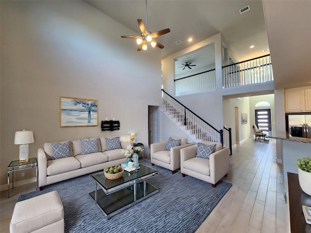 living area featuring visible vents, light wood-style flooring, a towering ceiling, stairway, and baseboards