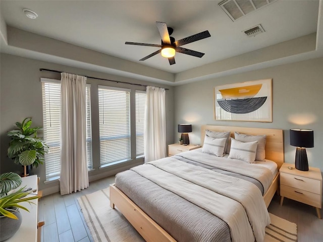 bedroom with a raised ceiling, visible vents, and light wood finished floors