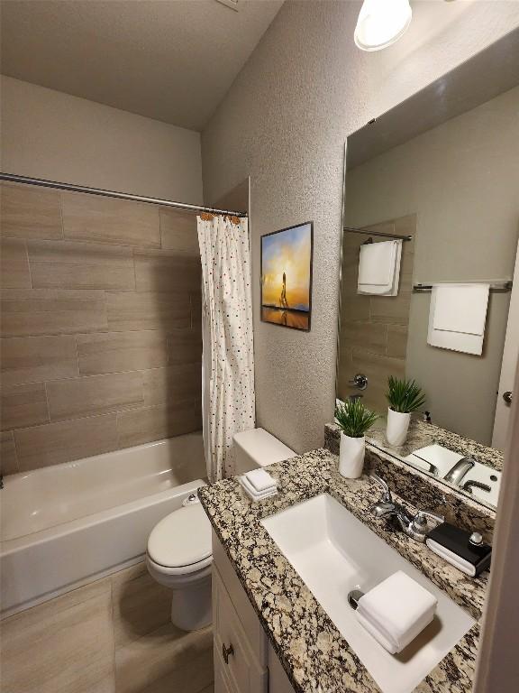 bathroom with toilet, vanity, shower / bath combination with curtain, and a textured wall