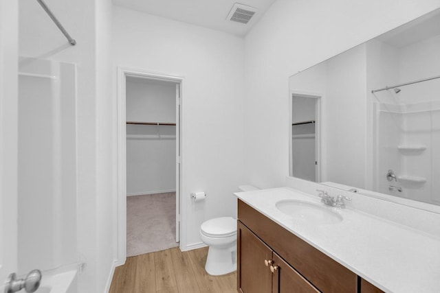 bathroom with visible vents, toilet, wood finished floors, a walk in closet, and vanity