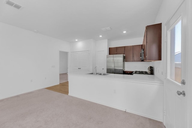 kitchen with light carpet, stainless steel appliances, a peninsula, a sink, and visible vents