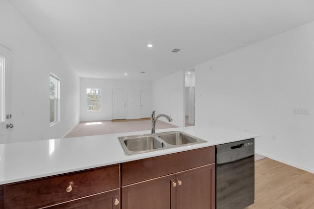 kitchen with light wood finished floors, black dishwasher, open floor plan, light countertops, and a sink