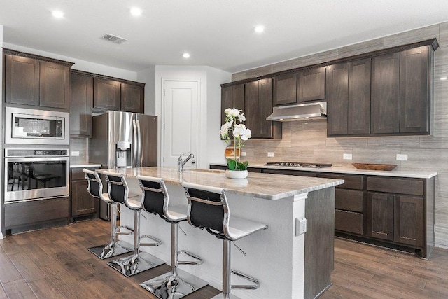 kitchen with dark brown cabinetry, under cabinet range hood, appliances with stainless steel finishes, and dark wood-style flooring