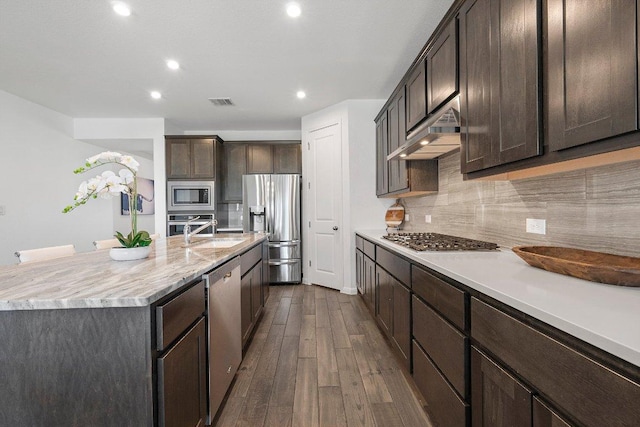 kitchen with dark brown cabinetry, decorative backsplash, dark wood-style floors, stainless steel appliances, and under cabinet range hood