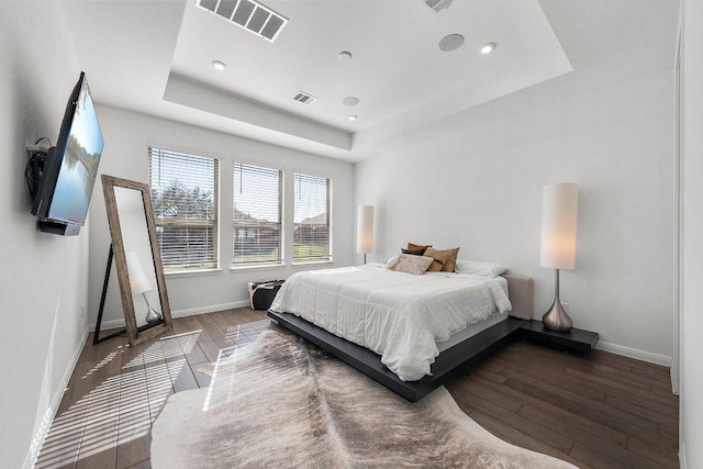 bedroom with hardwood / wood-style flooring, visible vents, a tray ceiling, and baseboards