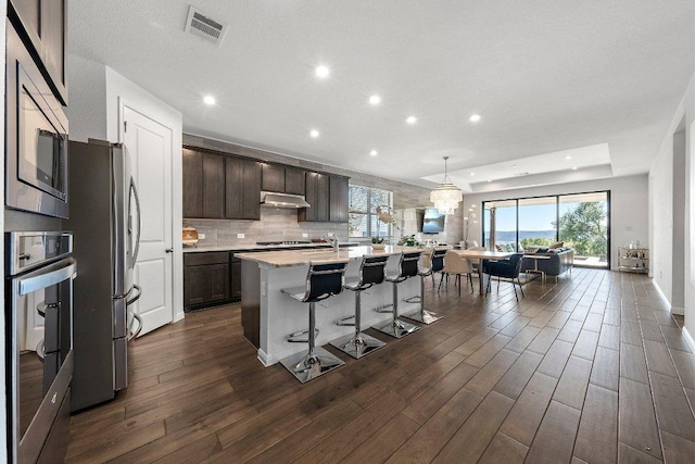 kitchen with under cabinet range hood, visible vents, stainless steel appliances, and dark wood-type flooring