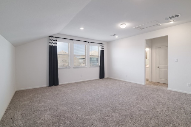 empty room featuring vaulted ceiling, light colored carpet, visible vents, and attic access