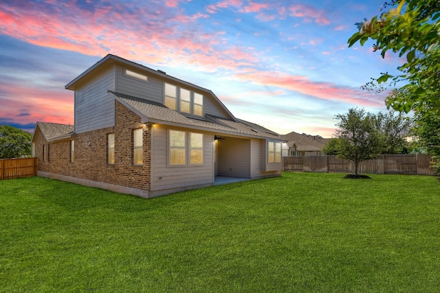 rear view of property with brick siding, a fenced backyard, and a yard