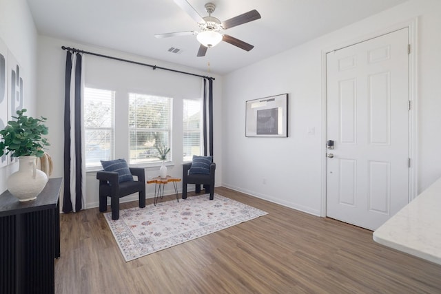 living area featuring ceiling fan, wood finished floors, visible vents, and baseboards