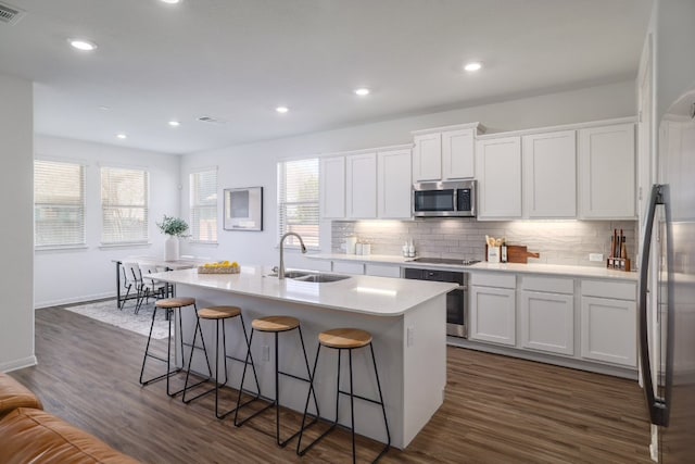 kitchen with dark wood-style floors, a breakfast bar area, appliances with stainless steel finishes, a sink, and backsplash