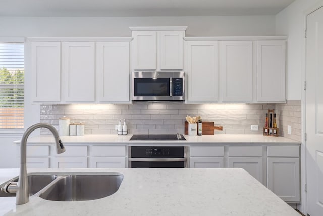 kitchen featuring stainless steel appliances, a sink, white cabinetry, and decorative backsplash