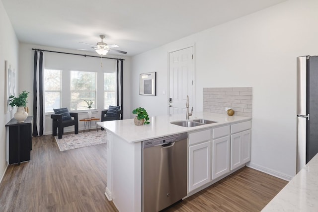 kitchen with wood finished floors, a peninsula, appliances with stainless steel finishes, and a sink