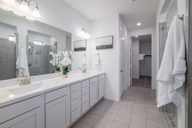 bathroom featuring double vanity, baseboards, a tile shower, and a sink