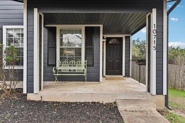 view of exterior entry featuring a porch and fence