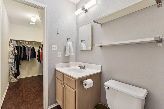 bathroom featuring a walk in closet, toilet, vanity, wood finished floors, and baseboards