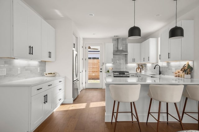 kitchen with light wood-type flooring, a sink, a peninsula, appliances with stainless steel finishes, and wall chimney exhaust hood