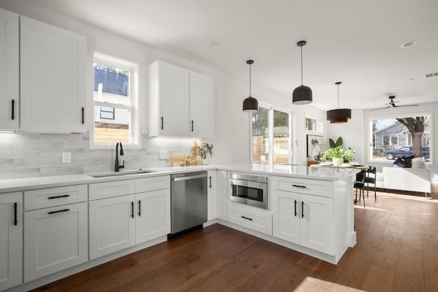 kitchen featuring dark wood-type flooring, dishwasher, decorative backsplash, a peninsula, and a sink