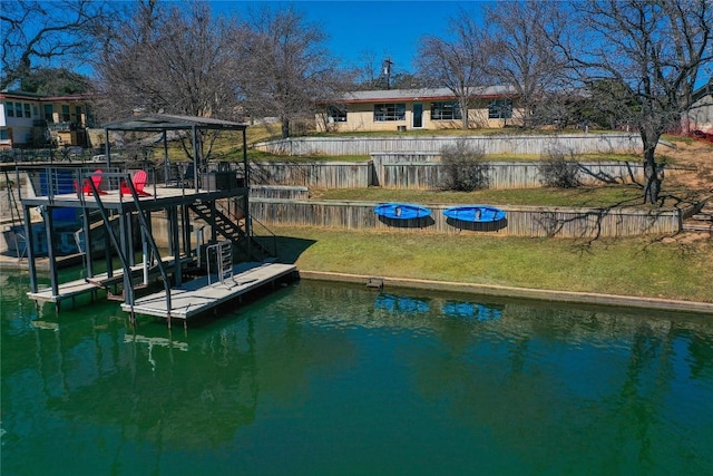 dock area with a water view, fence, and a lawn