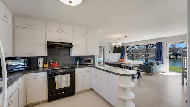 kitchen with a notable chandelier, dark countertops, a peninsula, under cabinet range hood, and black appliances